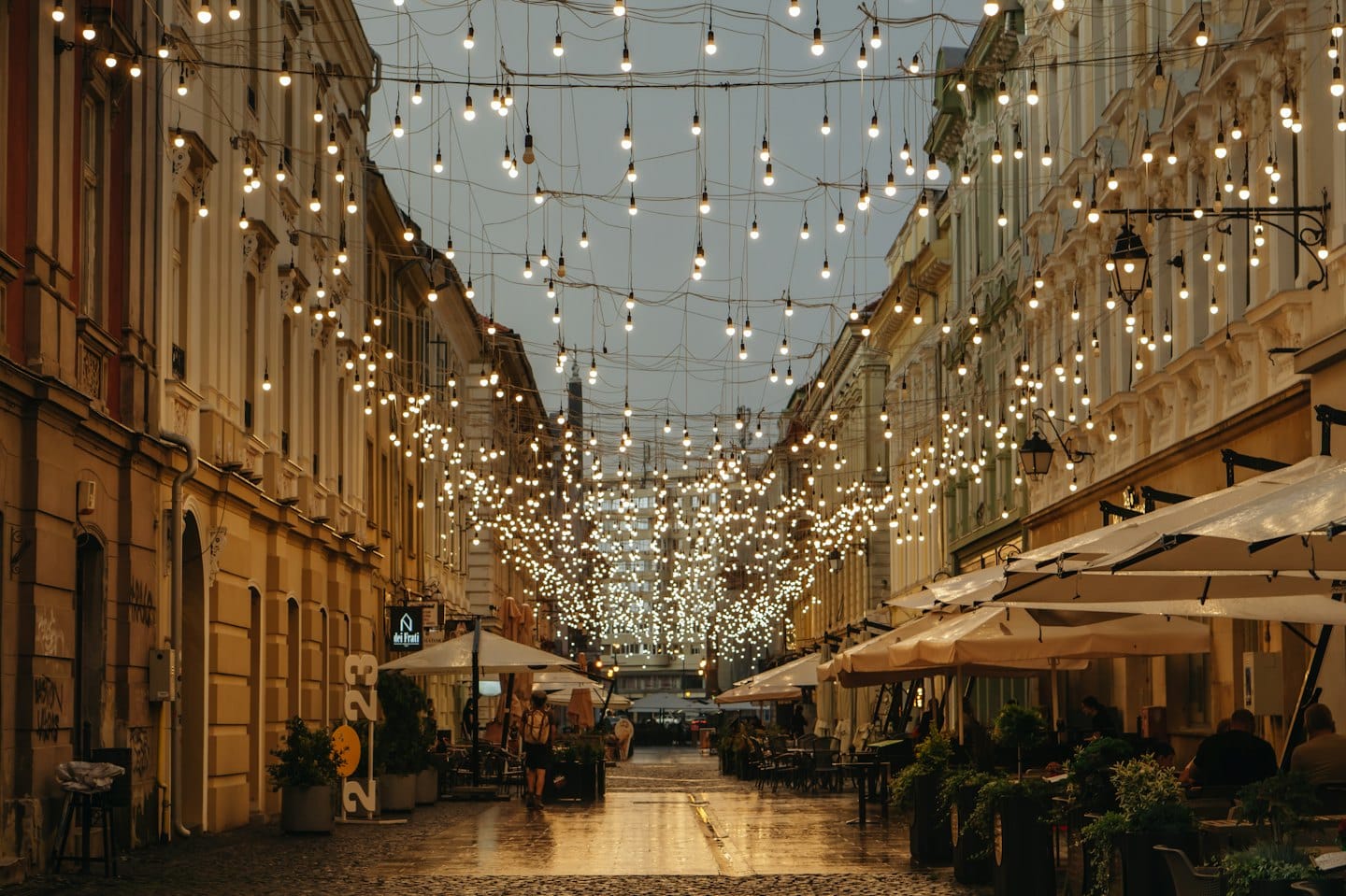Strada acciottolata di notte con luci a filo e tavoli all'aperto.